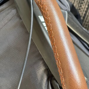 Pu&ograve; includere: Primo piano di un manubrio in pelle marrone con cuciture arancioni. Le cuciture sono un dettaglio decorativo sul manubrio.