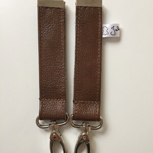 May include: Two brown leather straps with silver metal clasps. The straps are about 12 inches long and have a stitched seam down the center.