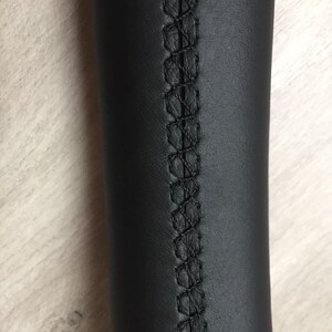 May include: Close-up of a black leather steering wheel cover with black stitching detail.