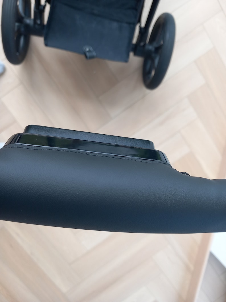 May include: A black stroller handlebar with a leather grip. The handlebar is made of metal and has a black finish. The leather grip is soft and comfortable to hold.