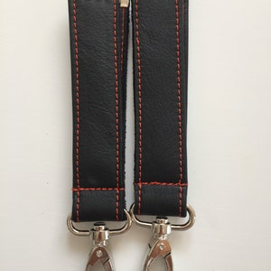 May include: Two black leather straps with orange stitching and silver metal clasps. The straps are about 10 inches long.
