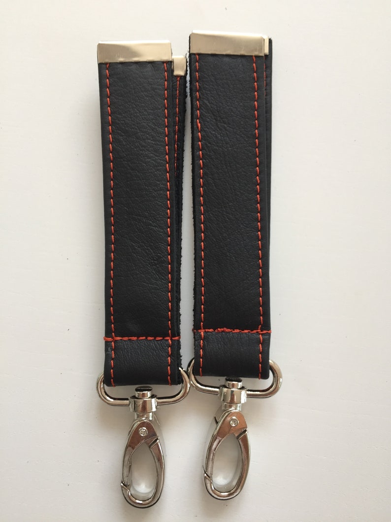 May include: Two black leather straps with orange stitching and silver metal clasps. The straps are about 10 inches long.