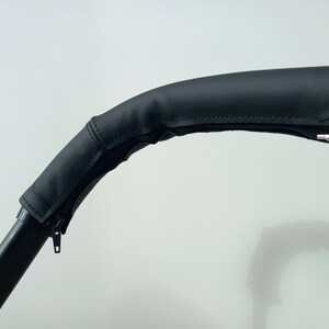 May include: Black leather handlebar cover with a zipper. The cover is designed to fit over a stroller handlebar.