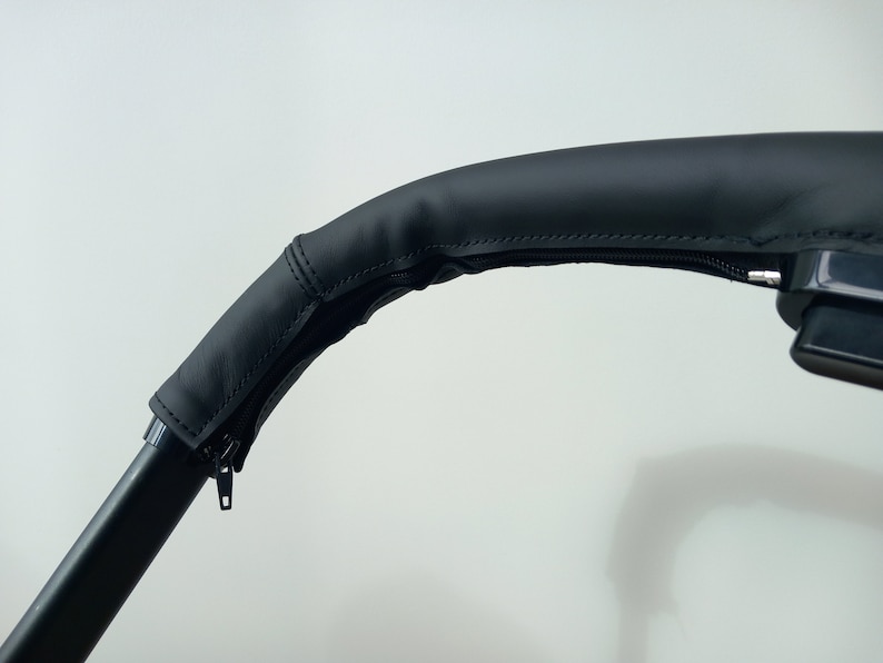 May include: Black leather handlebar cover with a zipper. The cover is designed to fit over a stroller handlebar.