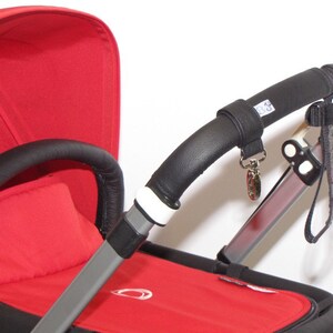 May include: A red stroller with a black leather handlebar and a black leather handle on the side. The stroller has a white strap with a silver buckle and a black strap with a silver buckle.