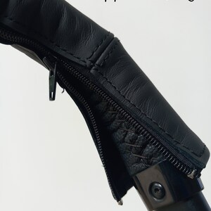 May include: Black leather zipper closure on a pushchair handle. The zipper is closed.