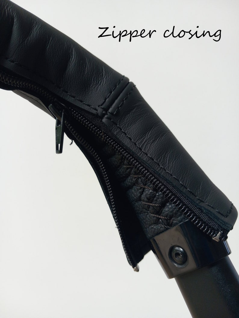 May include: Black leather zipper closure on a pushchair handle. The zipper is closed.