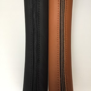 May include: Two zippered leather pouches, one black and one brown. Both pouches are closed and have a zipper running down the centre.
