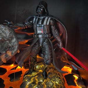 Peut inclure: Figurine détaillée de Dark Vador, vêtu de son armure et de son casque noirs emblématiques, avec un sabre laser rouge. La figurine se dresse sur une base dorée semblable à de la lave, avec un fond sombre. Objet de collection.
