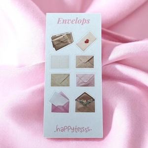 Op de afbeelding: Een rechthoekige sticker met het woord "Envelops" bovenaan. De sticker toont illustraties van verschillende enveloppen, waaronder een bruine papieren envelop, een witte envelop met een rood hart en een roze envelop. De tekst ".happytessss." staat onderaan.