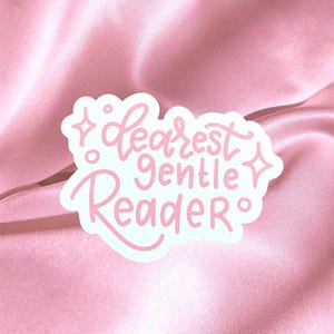 Op de afbeelding: Een witte sticker met de tekst "Dearest Gentle Reader" in roze, cursieve letters. De sticker heeft een wolkachtige vorm met decoratieve ster- en stipaccenten. De achtergrond is een roze satijnen stof.