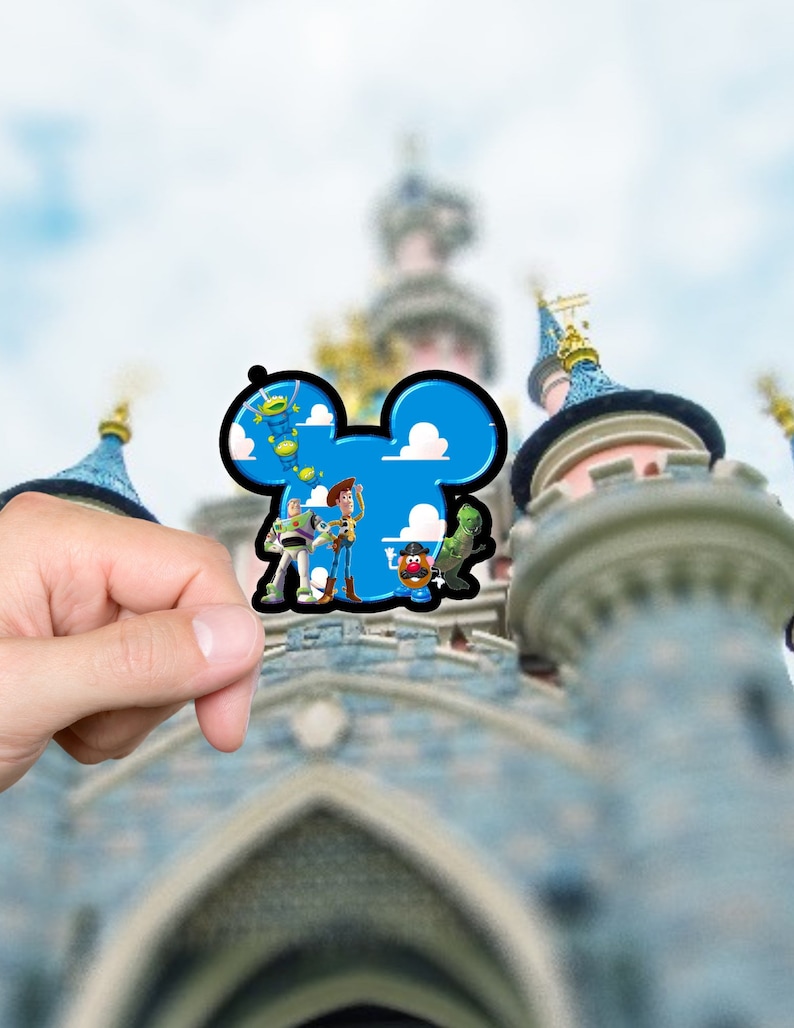 May include: A die-cut sticker shaped like a mouse head silhouette featuring a blue sky background with white clouds. The sticker displays animated characters including a space ranger, a cowboy, a potato-shaped figure, and a green dinosaur.