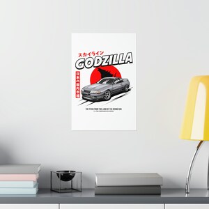 May include: A white graphic tee with a silver car and a red circle with a Godzilla silhouette. The text "スカイライン GODZILLA 日本の国内市場 THE TITAN FROM THE LAND OF THE RISING SUN" is printed on the shirt.