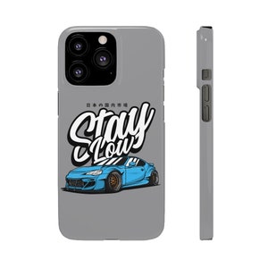 May include: A gray iPhone case with a blue car illustration and the text "Stay Low" in white. The Japanese text "日本の国内市場" is also included on the case.