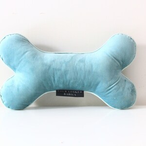 May include: A light blue plush dog bone pillow with white piping and the text "Four Legged Babies" on the bottom.