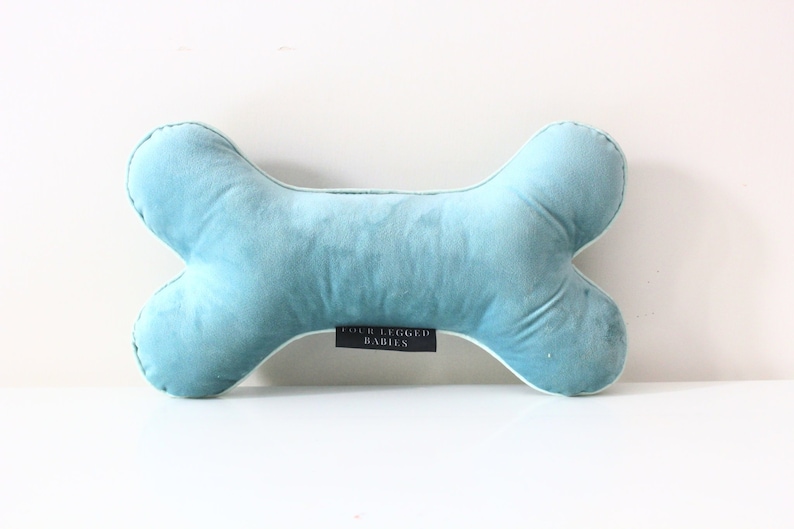 May include: A light blue plush dog bone pillow with white piping and the text "Four Legged Babies" on the bottom.