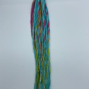 May include: A set of blue, pink, and green synthetic dreadlocks with gold glitter strands. The dreadlocks are tied together with a green rubber band.