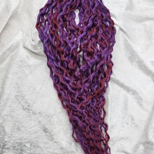 May include: A bundle of long, curly synthetic hair extensions in shades of purple and burgundy.