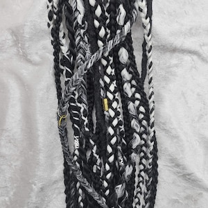 May include: A set of black and white synthetic hair extensions. The extensions are braided and have a textured look.