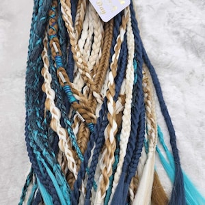 May include: A bundle of blue, teal, brown, and white synthetic hair extensions. The extensions are braided and have a variety of textures. The extensions are packaged with a small card that says "You Got This!" and "Blessed & Kindred".