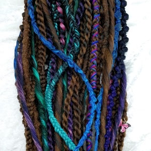 May include: A bundle of brown, blue, teal, purple, and green synthetic dreadlocks with a butterfly charm.