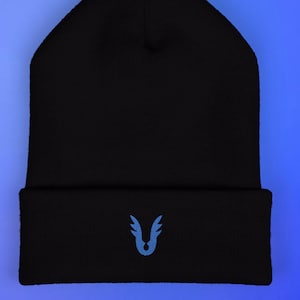 May include: Black beanie with a folded brim. The beanie features a light blue embroidered design of a stylized wing or feather on the folded brim. The background is a gradient of blue.