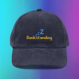 May include: Navy blue corduroy baseball cap with the word "Bankstanding" embroidered in yellow and blue. The design includes the letter "Z" and the word "Bankstanding" in a playful font.