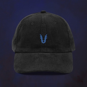 May include: Black corduroy baseball cap with a curved brim. The cap features a small, embroidered blue emblem on the front. The hat has a classic six-panel design with a top button and an adjustable strap at the back.