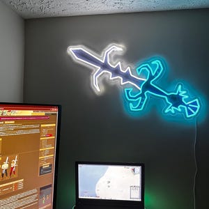 May include: A neon sign shaped like a sword with a blue and white glow. The sign is mounted on a wall above a desk with a laptop and a desktop computer.