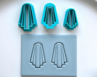 May include: A set of three teal-colored ghost-shaped cookie cutters in varying sizes, along with a light blue silicone mold featuring two ghost shapes. The cutters and mold are arranged on a white surface, perfect for Halloween-themed baking.