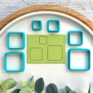 May include: A selection of square cookie cutters in different sizes and a textured green fondant piece. The cutters are a bright teal colour, and the fondant piece has three square indentations. The items are arranged on a white surface.