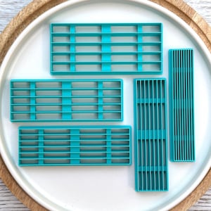 May include: A set of five teal plastic rectangular cookie cutters featuring grid patterns. Three cutters have horizontal and vertical bars forming a square grid, while two longer, narrower cutters feature closely spaced vertical bars.