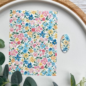 Könnte beinhalten: Ein Blumenmuster mit bunten Blumen in Rosa, Blau, Gelb und Orange auf weißem Hintergrund. Ein ovales Objekt mit passendem Blumendesign ist ebenfalls vorhanden. Das Design befindet sich auf einem weißen Tablett.