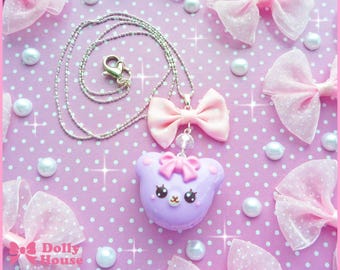 May include: A purple bear charm necklace with a pink bow and silver chain. The necklace is on a pink background with white polka dots.