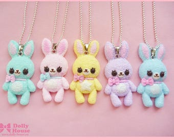 May include: Five pastel-colored bunny charm necklaces. The bunnies are made of a soft, fuzzy material and have pink, blue, yellow, purple, and light blue fur. Each bunny has a small pink bow tied around its neck.