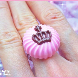 K&ouml;nnte beinhalten: Ein rosa Ring mit einem braunen Kronendesign. Der Ring ist spiralf&ouml;rmig und hat eine gl&auml;nzende Oberfl&auml;che.