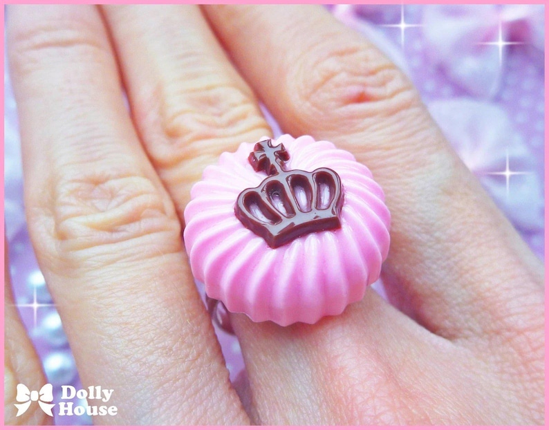 K&ouml;nnte beinhalten: Ein rosa Ring mit einem braunen Kronendesign. Der Ring ist spiralf&ouml;rmig und hat eine gl&auml;nzende Oberfl&auml;che.
