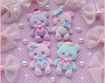 May include: A collection of pastel-colored bear figurines with bows and decorative accents. The bears are in shades of pink, blue, and purple, with pearl embellishments and matching bows. The background is a pink polka-dot pattern.
