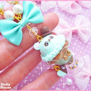 May include: A light blue and white charm necklace with a green and brown ice cream cone charm. The charm features a cute cartoon face with black eyes and a brown hat. The necklace is made of beads and a gold chain.