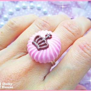 K&ouml;nnte beinhalten: Rosa Ring mit einem braunen Kronendesign. Der Ring ist in Form eines Zuckerguss-Wirbels geformt.