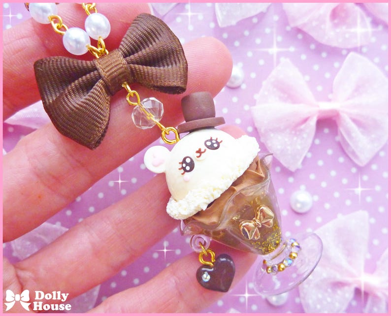 May include: A brown bow with a gold chain and a white and brown ice cream charm with a bunny face. The charm is in a clear glass container with gold glitter and a heart-shaped charm.