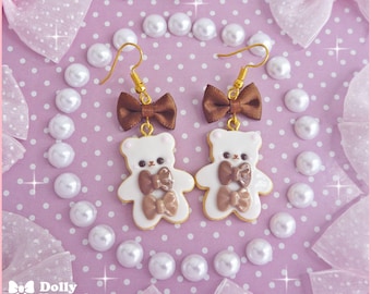 May include: A pair of earrings featuring white bear charms with brown bow accents. The bears are wearing brown bows and the earrings have brown bows hanging from the top.