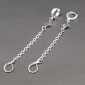 May include: A pair of silver hoop earrings with a dangling chain and star charm.
