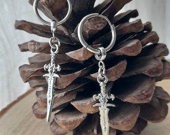 May include: A pair of silver hoop earrings with sword charms. The swords have intricate details and a pointed tip.