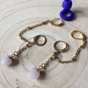 Peut inclure: Boucles d'oreilles doubles en chaîne dorée avec des pierres précieuses roses pâles. Les boucles d'oreilles sont dotées d'une fermeture à levier et d'un design de chaîne délicat. Un petit objet violet en forme d'anneau est en arrière-plan.