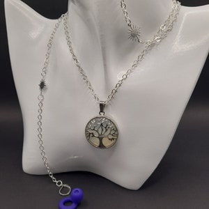 May include: A silver necklace with a tree of life pendant. The pendant is round and has a white and green design. The necklace also has two smaller silver stars.