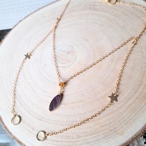 May include: A gold chain necklace with a purple stone pendant and star charms. The necklace is layered and has two chains.