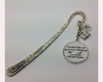 May include: Silver bookmark featuring a quote from Jane Austen's Pride and Prejudice: "I declare after all there is no enjoyment like reading!" The bookmark has a charm with the letter T and a charm with a book.