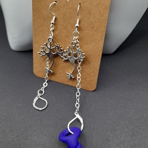 May include: A pair of silver earrings with a neuron design. The earrings are hanging from a silver chain and have a small blue silicone stopper at the end.
