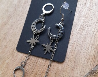 May include: Silver-toned dangle earrings featuring crescent moons and star charms. The earrings hang from a chain and have a lever-back closure. The earrings are displayed on a black card with the words "Handmade with love".